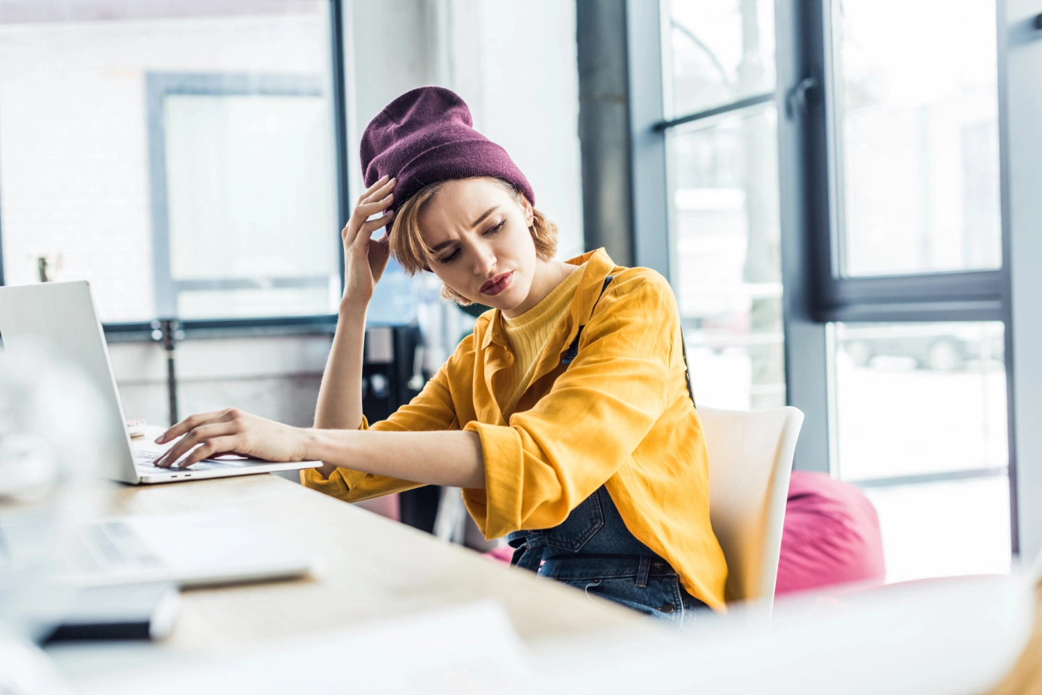 Cover: 5 typische Marketing-Fehler von Designern: Man sieht eine junge Frau vor ihrem Laptop an einem Schreibtisch sitzen. Sie macht ein frustriertes Gesicht und guckt genervt zur Seite.